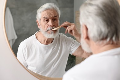Photo of Senior man combing mustache near mirror in bathroom