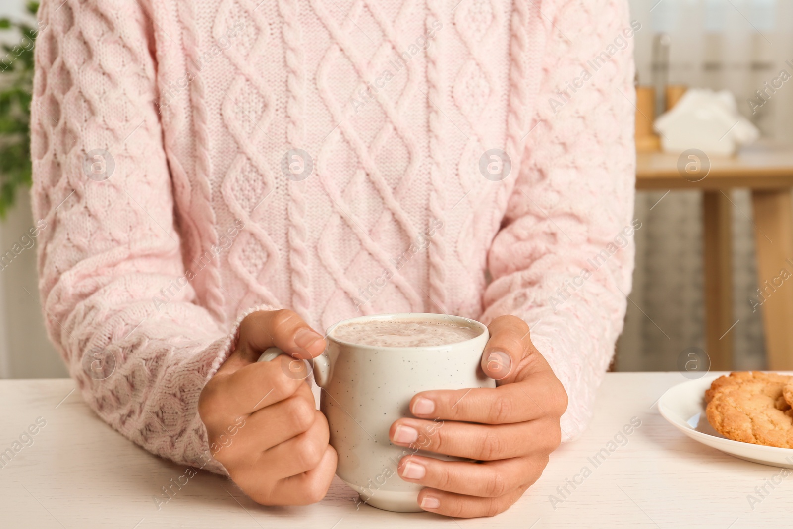 Photo of Woman holding cup of delicious cocoa drink at white table, closeup