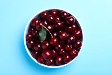 Photo of Sweet juicy cherries with leaf on light blue background, top view