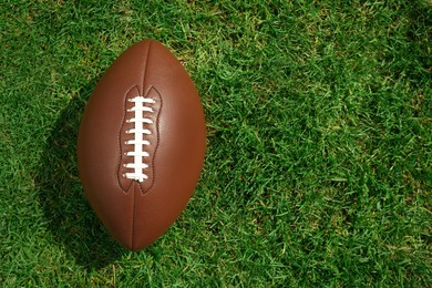 Photo of American football ball on green grass, top view. Space for text