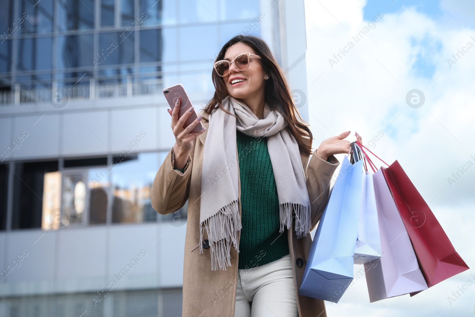 Photo of Beautiful young woman with shopping bags and smartphone outdoors