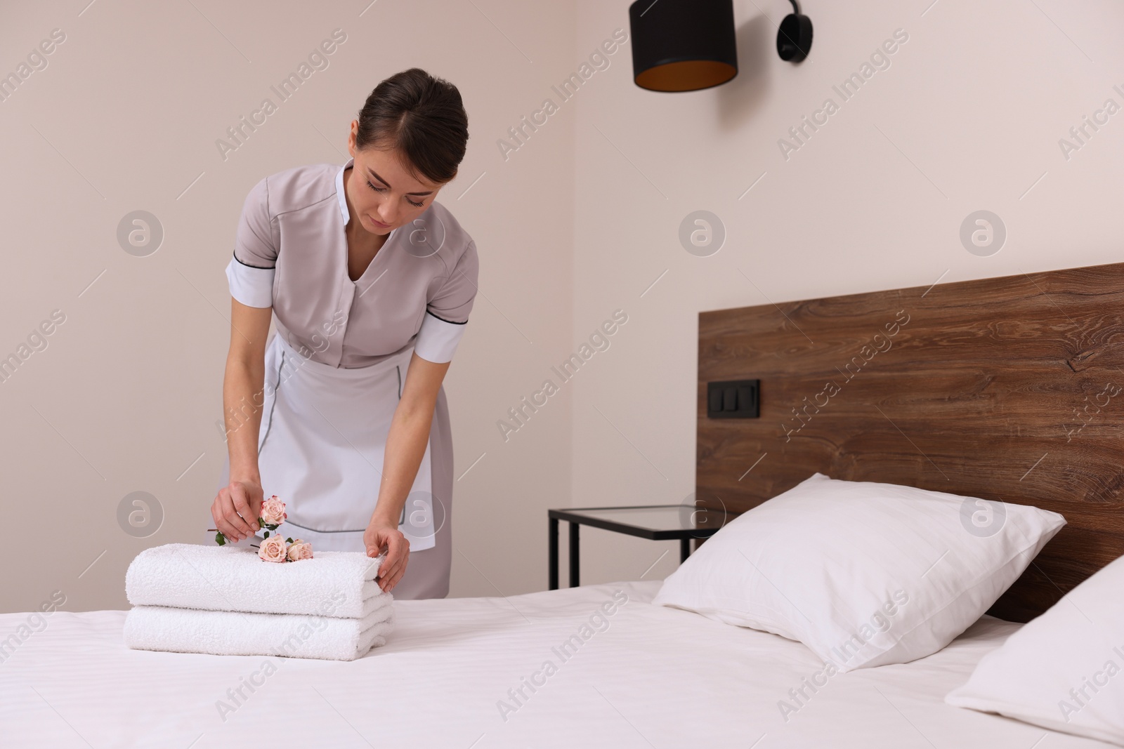 Photo of Beautiful chambermaid putting flowers on fresh towels in hotel room