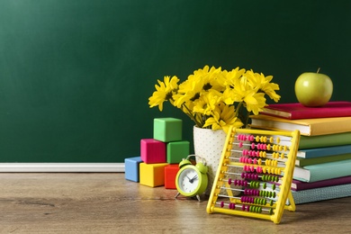 Vase of flowers, books and toys on wooden table near green chalkboard, space for text. Teacher's day