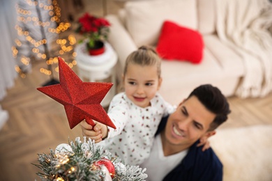 Father and little daughter decorating Christmas tree indoors, focus on star topper