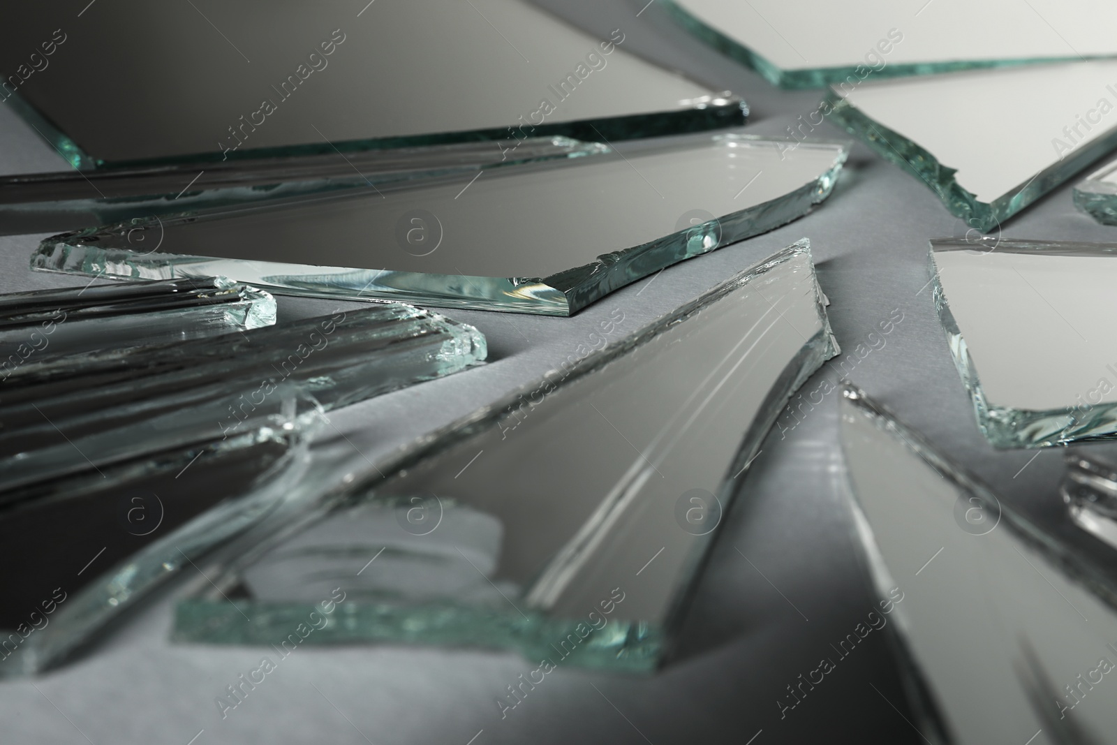 Photo of Shards of broken mirror on grey background, closeup