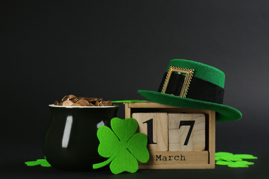 Photo of Composition with pot of gold coins and wooden block calendar on black background. St. Patrick's Day celebration