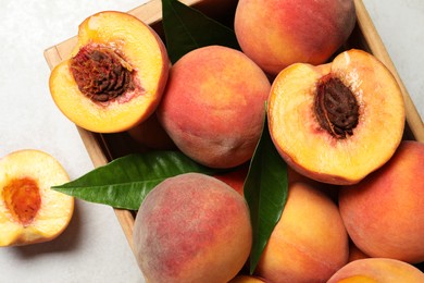 Photo of Delicious juicy peaches and leaves on light grey textured table, top view