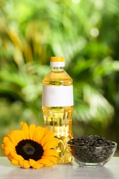 Photo of Sunflower cooking oil, seeds and yellow flower on light grey table outdoors