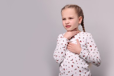 Girl suffering from sore throat on light grey background. Space for text