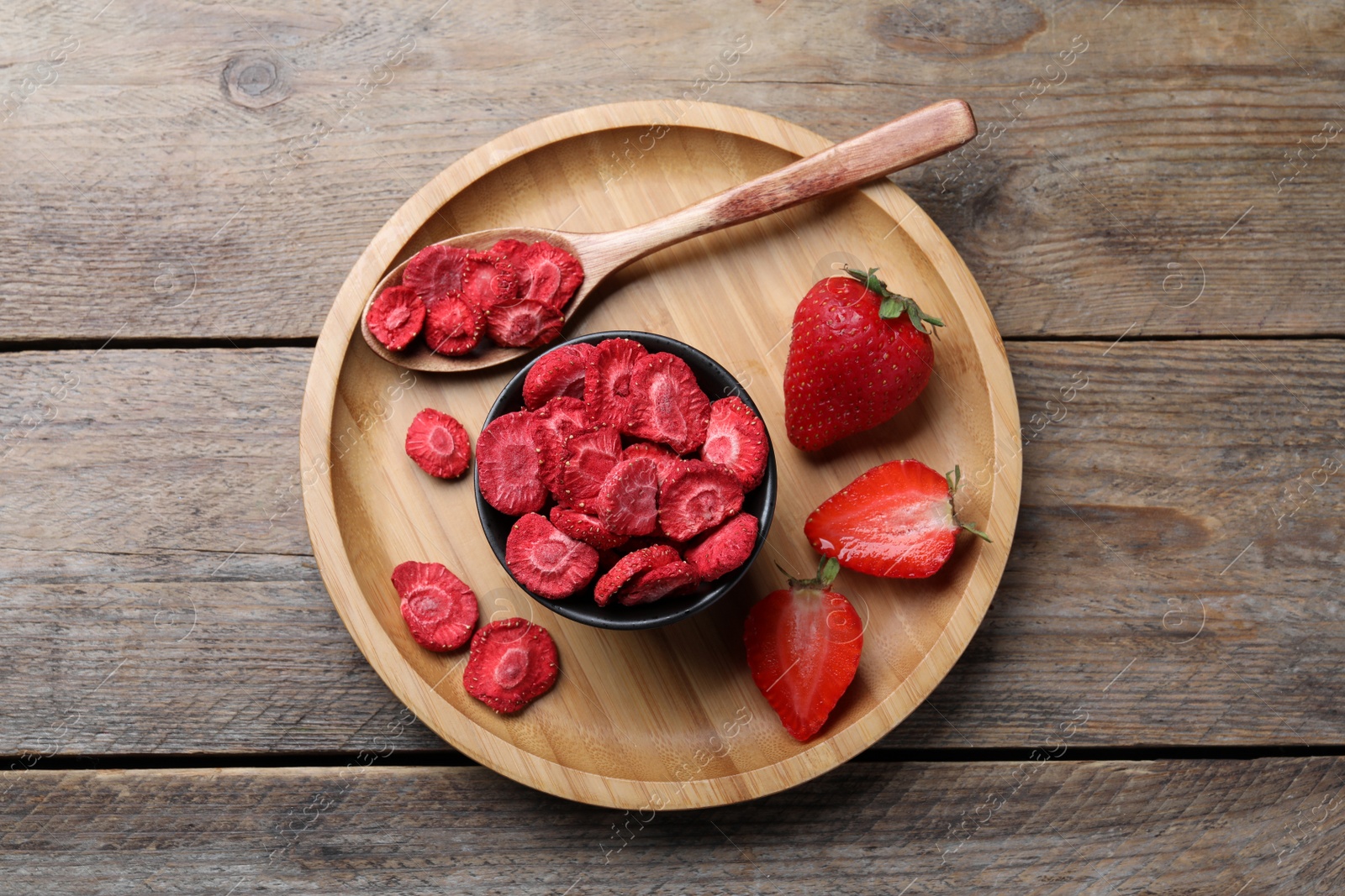 Photo of Freeze dried and fresh strawberries on wooden table, top view