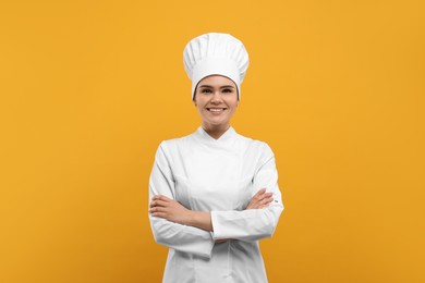 Photo of Happy female chef wearing uniform and cap on orange background