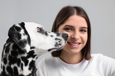 Photo of Beautiful woman with her adorable Dalmatian dog on light grey background, selective focus. Lovely pet