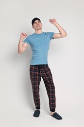 Happy man in pyjama and sleep mask stretching on light grey background