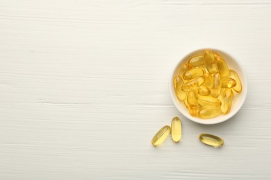 Photo of Vitamin capsules in bowl on white wooden table, top view. Space for text