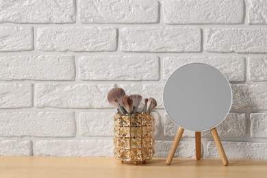 Mirror and makeup brushes on wooden dressing table in room. Space for text