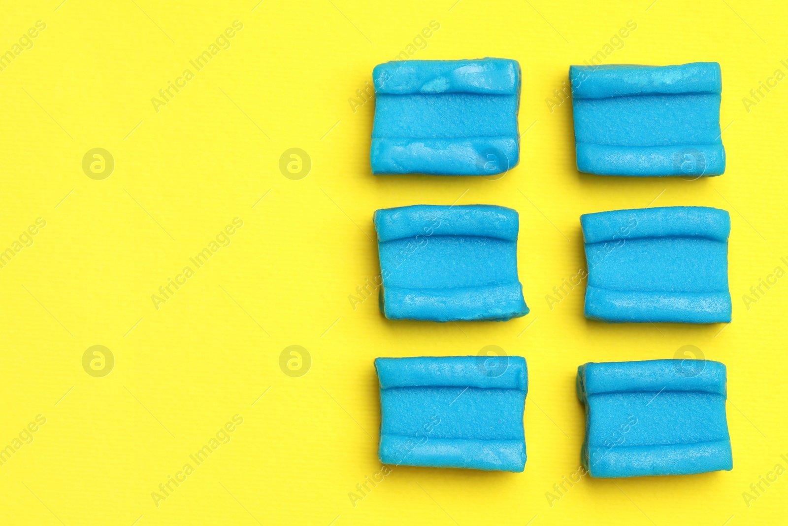 Photo of Blue bubble gums on yellow background, flat lay. Space for text