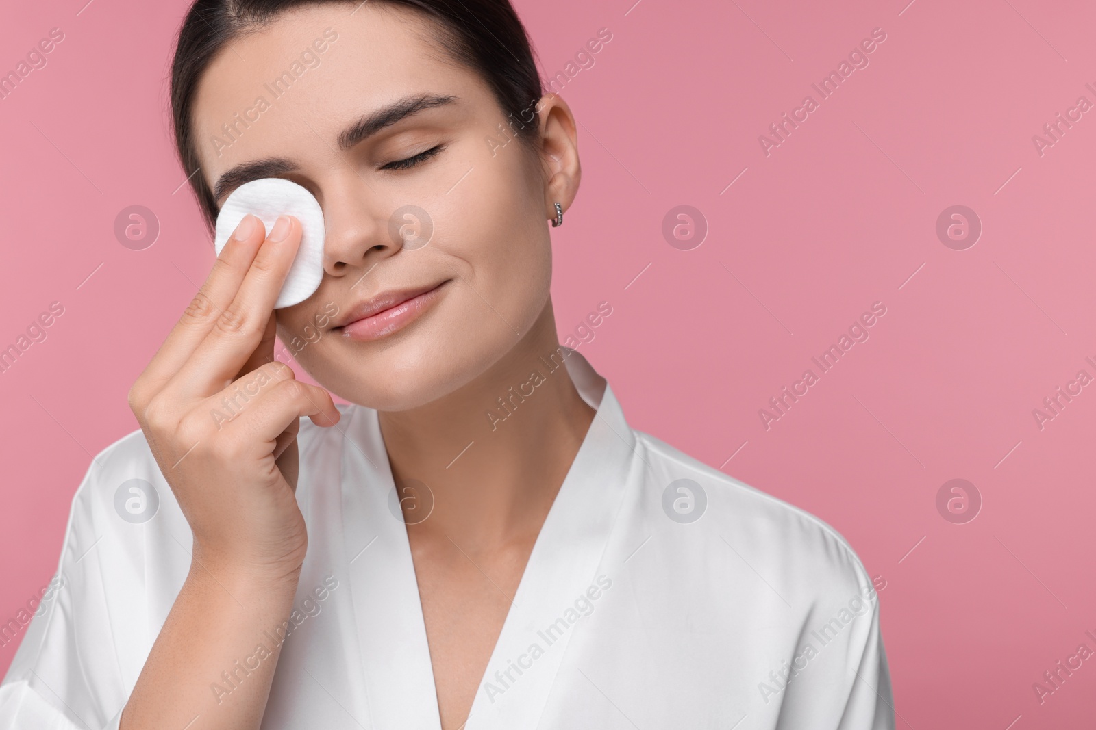 Photo of Young woman cleaning her face with cotton pad on pink background. Space for text