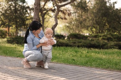 Mother teaching her baby how to walk outdoors. Space for text