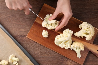Photo of Woman cutting fresh cauliflower at wooden table, top view