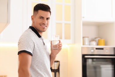 Man holding glass of pure water in kitchen. Space for text