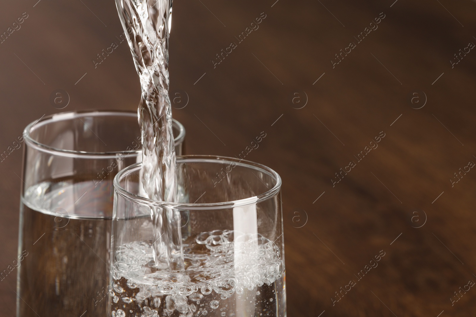 Photo of Pouring water into glass against blurred background, closeup. Space for text