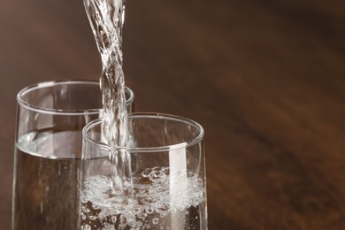 Pouring water into glass against blurred background, closeup. Space for text