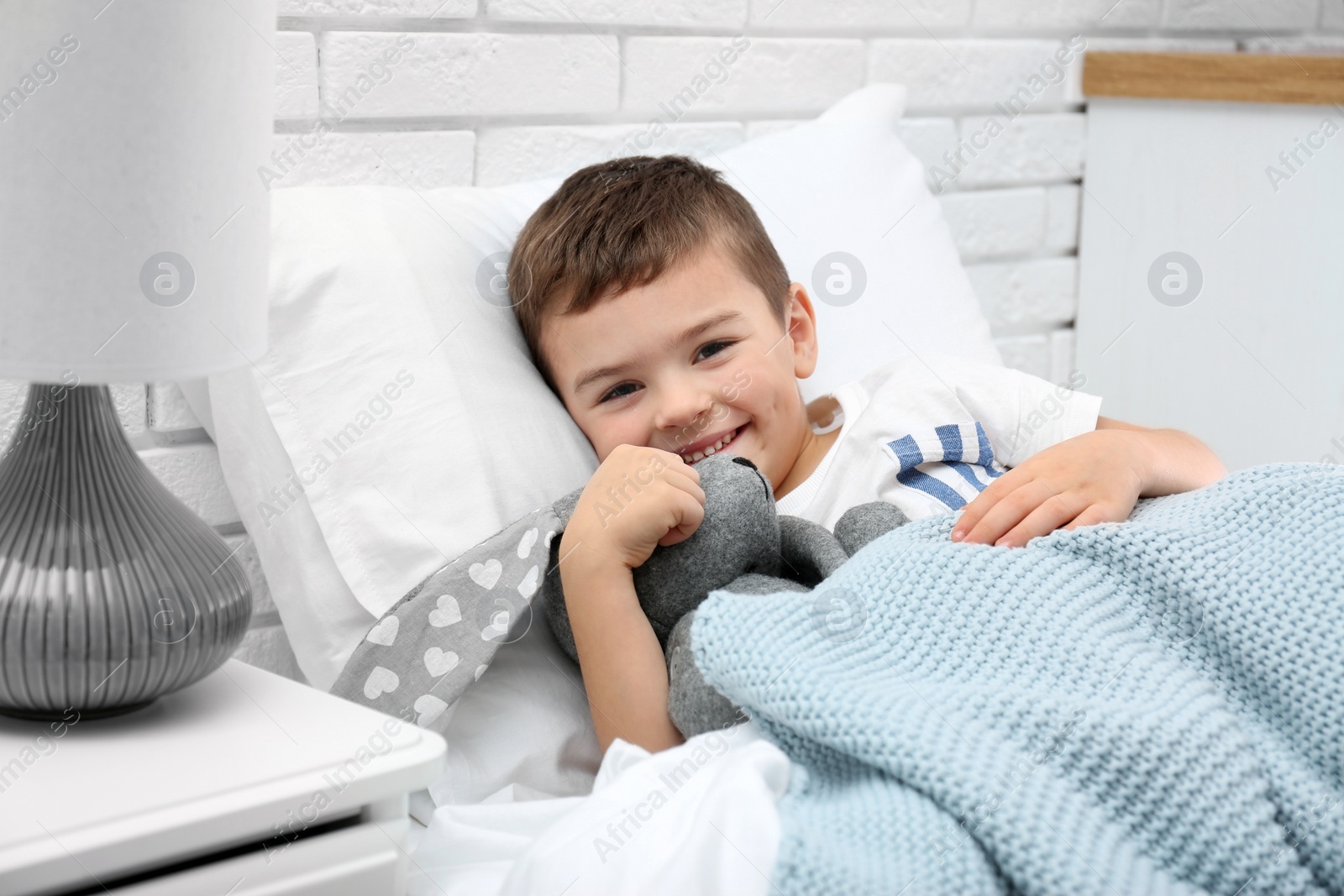 Photo of Cute child with stuffed bunny resting in bed at hospital