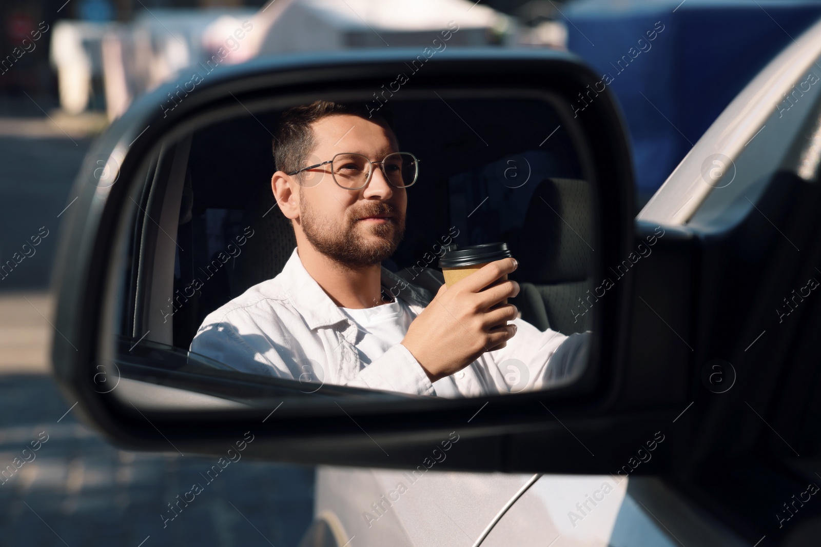 Photo of Coffee to go. Handsome man with paper cup of drink, view through car side mirror