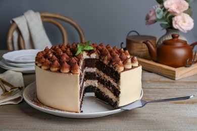 Photo of Delicious tiramisu cake with mint leaves and server on wooden table