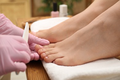 Photo of Professional pedicurist filing client`s toenails in beauty salon, closeup