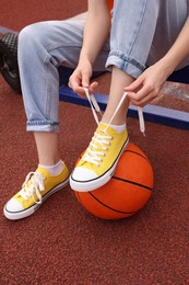 Photo of Woman tying shoelace of yellow classic old school sneaker on basketball ball at outdoor court, closeup