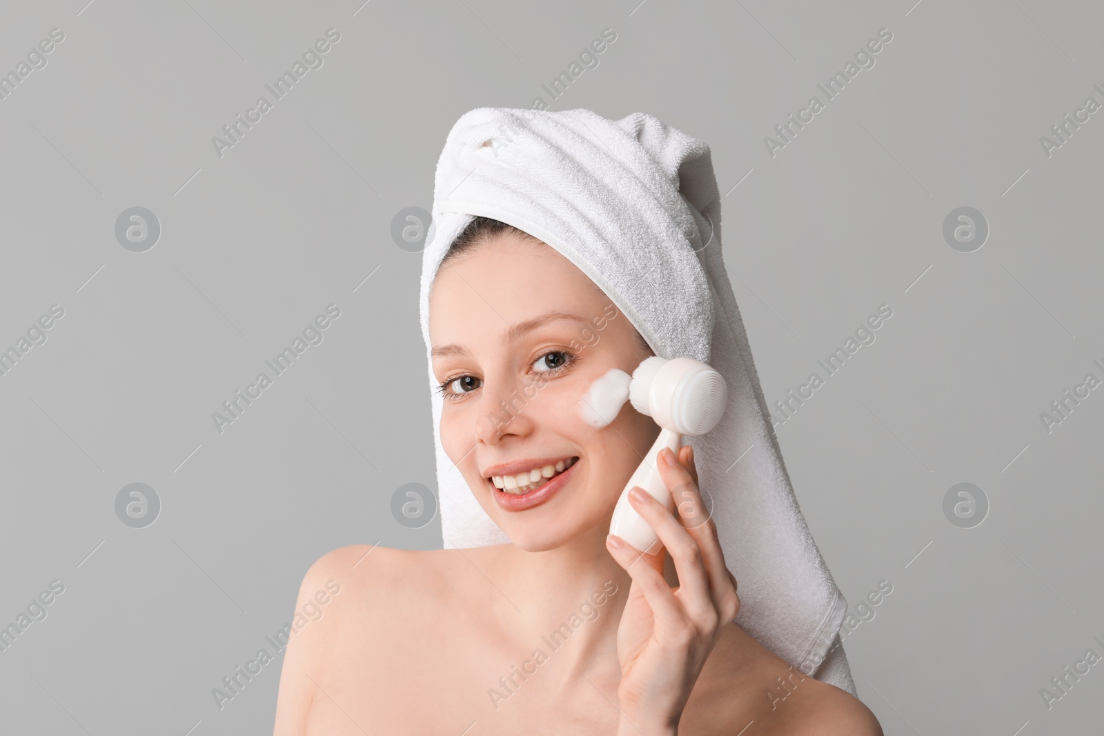 Photo of Young woman washing face with brush and cleansing foam on grey background