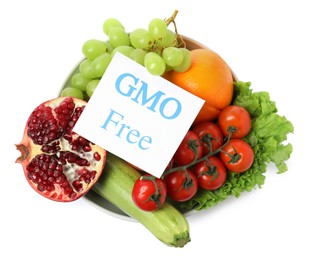 Fresh fruits, vegetables and card with text GMO Free in bowl on white background, top view