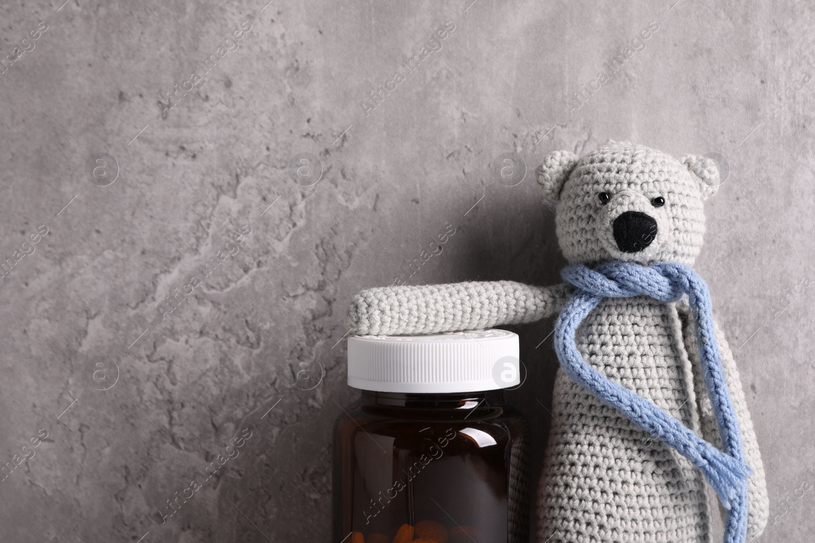 Photo of Toy bear and bottle of pills near grey wall, space for text