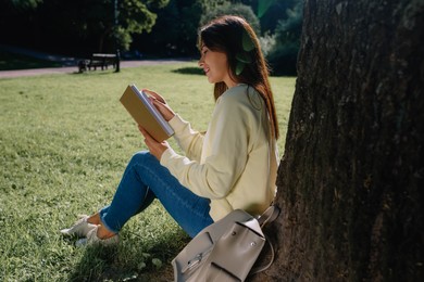 Photo of Young woman reading book near tree in park on sunny day