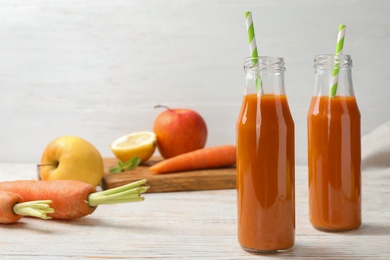Bottles of fresh carrot juice and ingredients on white wooden table, space for text