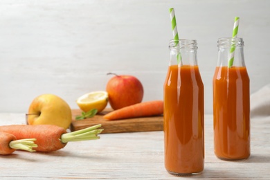 Photo of Bottles of fresh carrot juice and ingredients on white wooden table, space for text