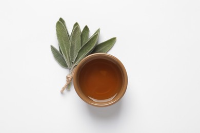 Bowl of essential sage oil and twig on white background, top view