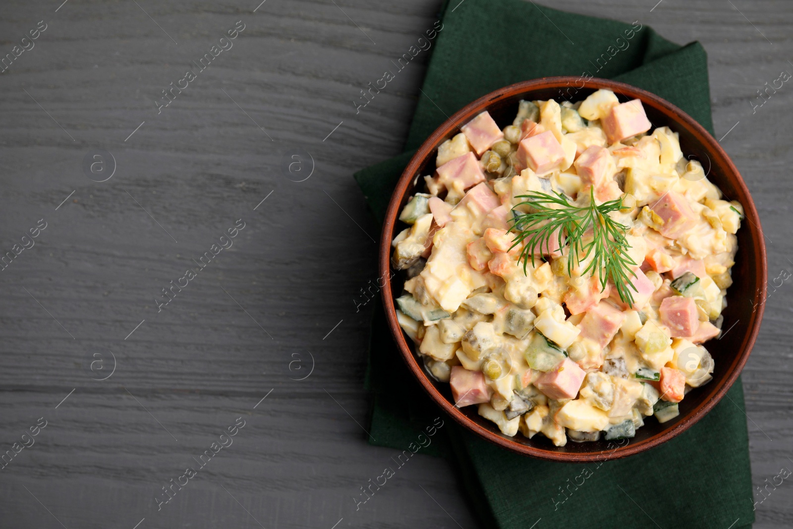 Photo of Tasty Olivier salad with boiled sausage in bowl on grey wooden table, top view. Space for text