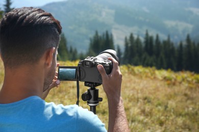 Photo of Man taking photo of nature with modern camera on stand outdoors