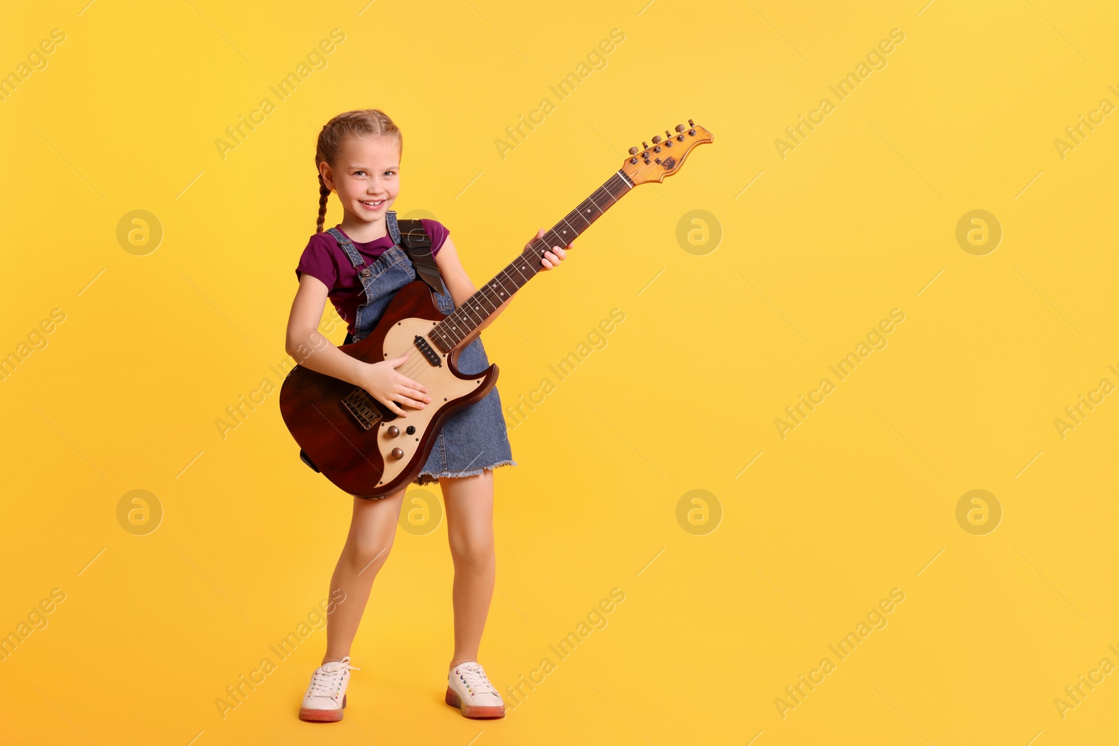 Photo of Cute girl with electric guitar on orange background