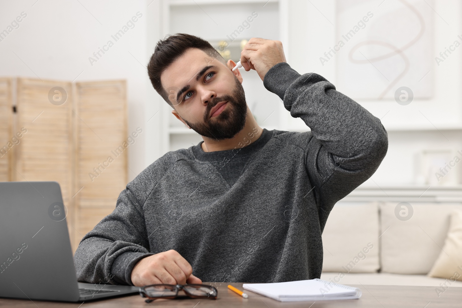 Photo of Young man applying medical ear drops at table indoors