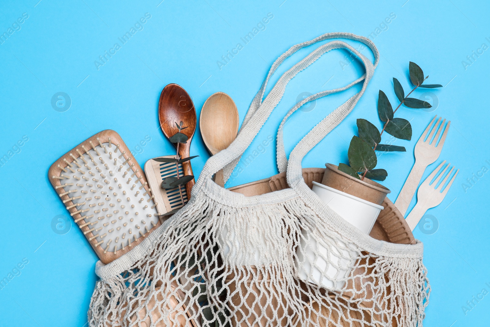 Photo of Net bag with different eco items on light blue background, top view. Recycling concept