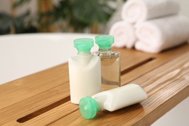 Wooden tray with mini bottles of cosmetic products on bath tub in bathroom