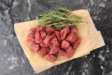 Photo of Pieces of raw beef meat and rosemary on grey textured table, top view