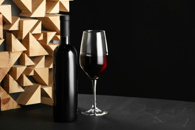 Stylish presentation of red wine in bottle and wineglass on table against black background, space for text