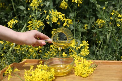 Woman pouring rapeseed oil from jug into bowl at tray outdoors, closeup