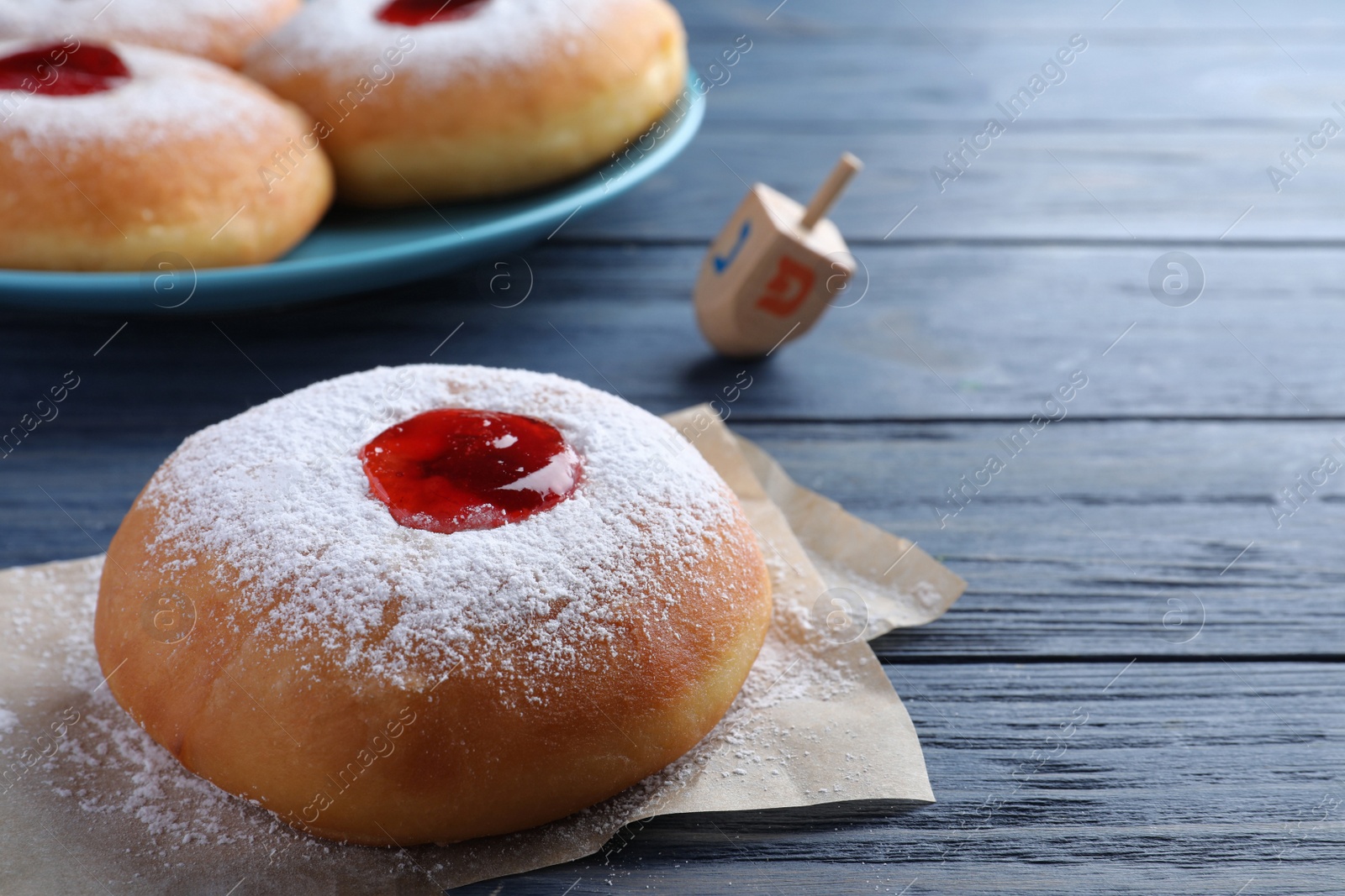 Photo of Hanukkah doughnut with jelly and sugar powder on blue wooden table, closeup. Space for text