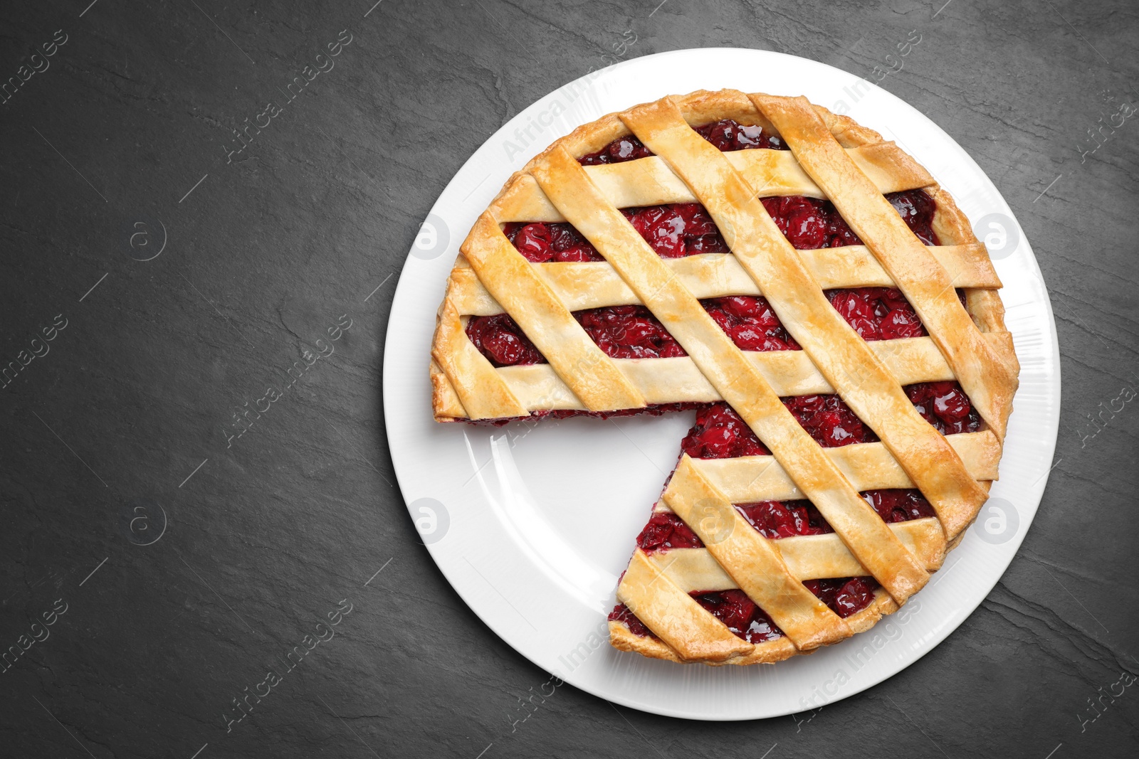 Photo of Delicious fresh cherry pie on black slate table, top view. Space for text