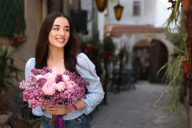 Beautiful woman with bouquet of spring flowers on city street, space for text